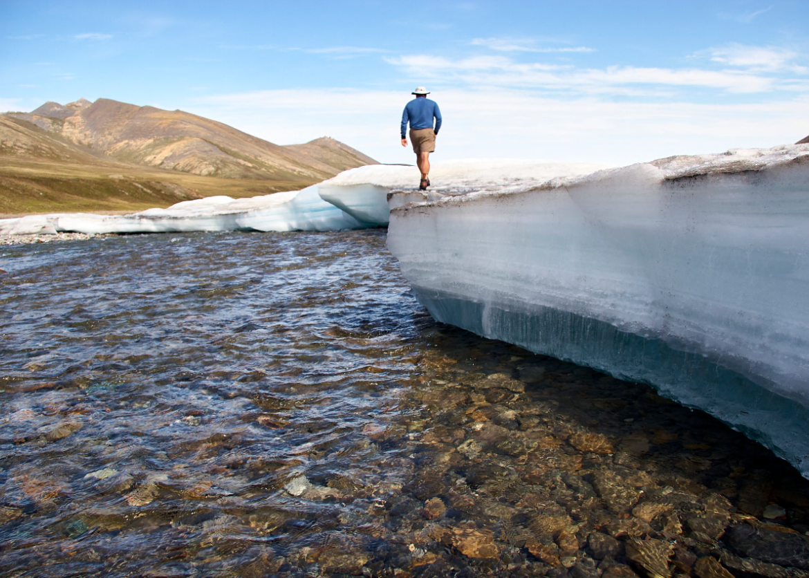 A man walking on an iceberg next to a river.