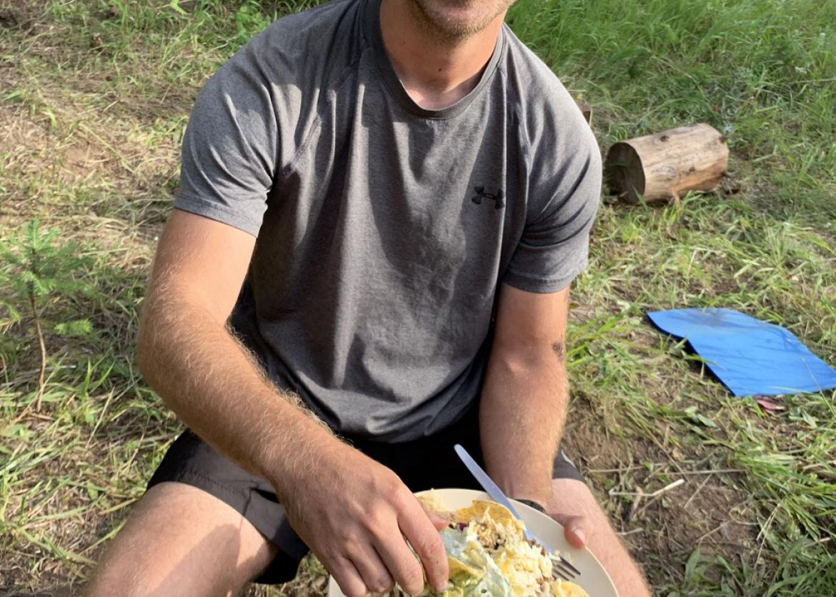 A man smiling and showing his plate of tacos.