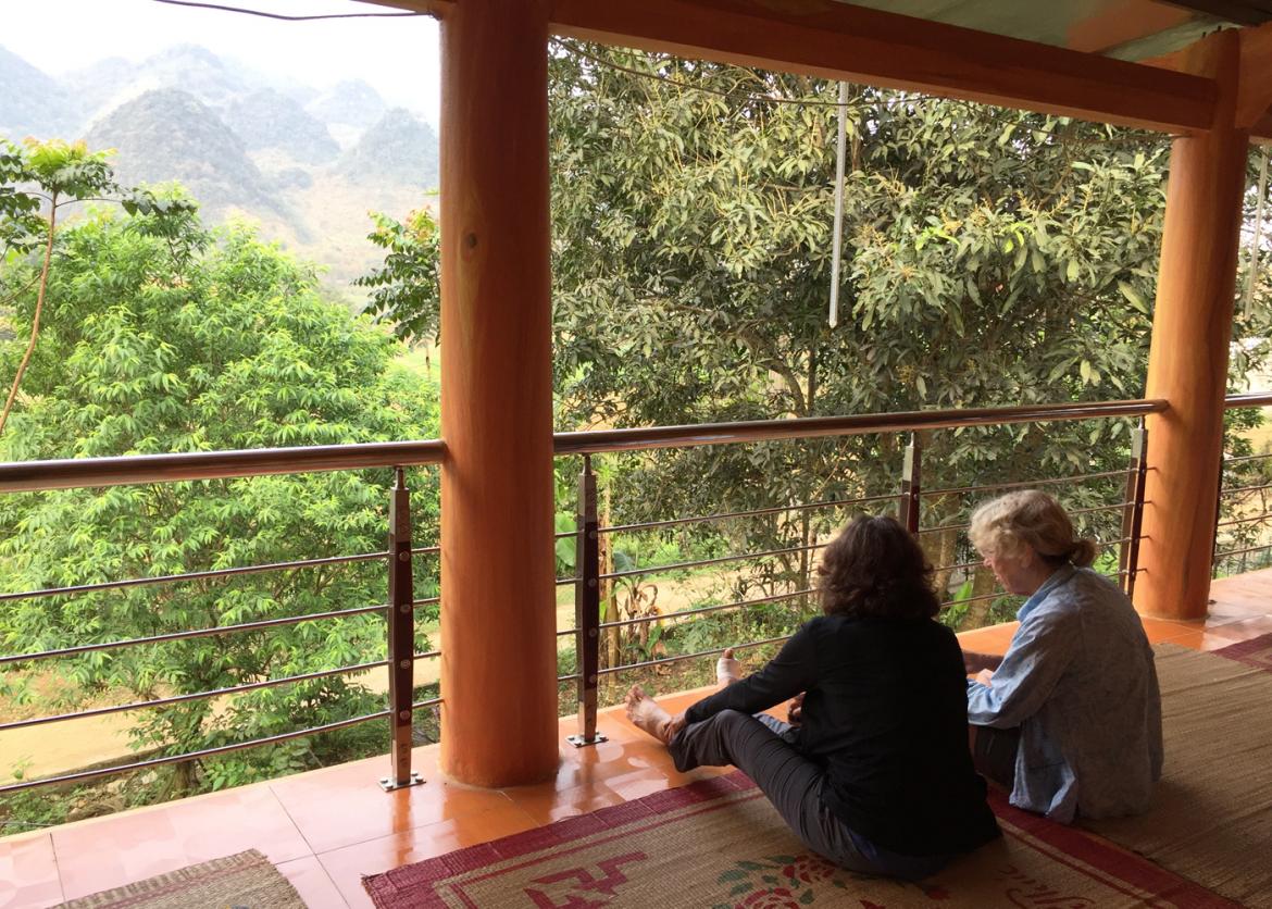 Two people sit in an open air terrace overlooking the the tops of trees.