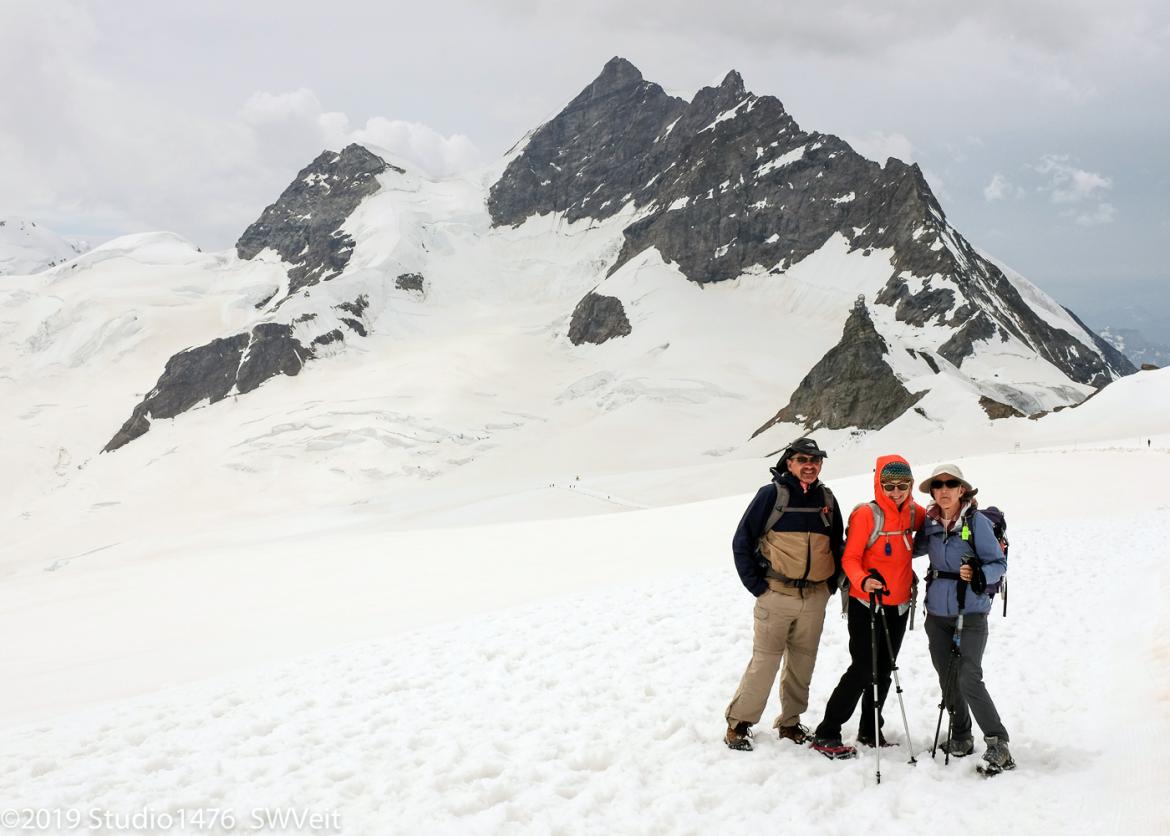 Three smiling hikers on snowy ground.