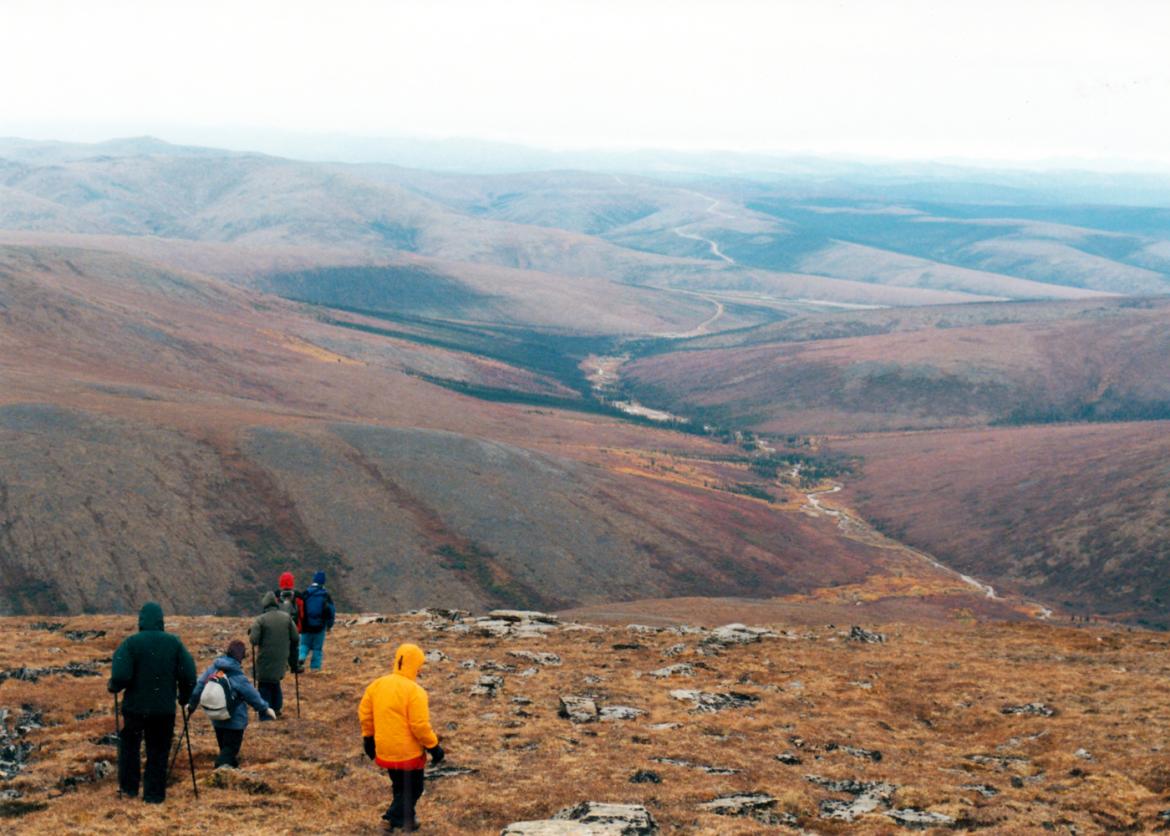 Participants trek, some with hiking poles, across a hillside with a view of flat red-brown hills.