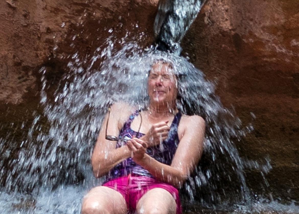 Woman sitting under small waterfall in Descent into Dark Canyon, Utah