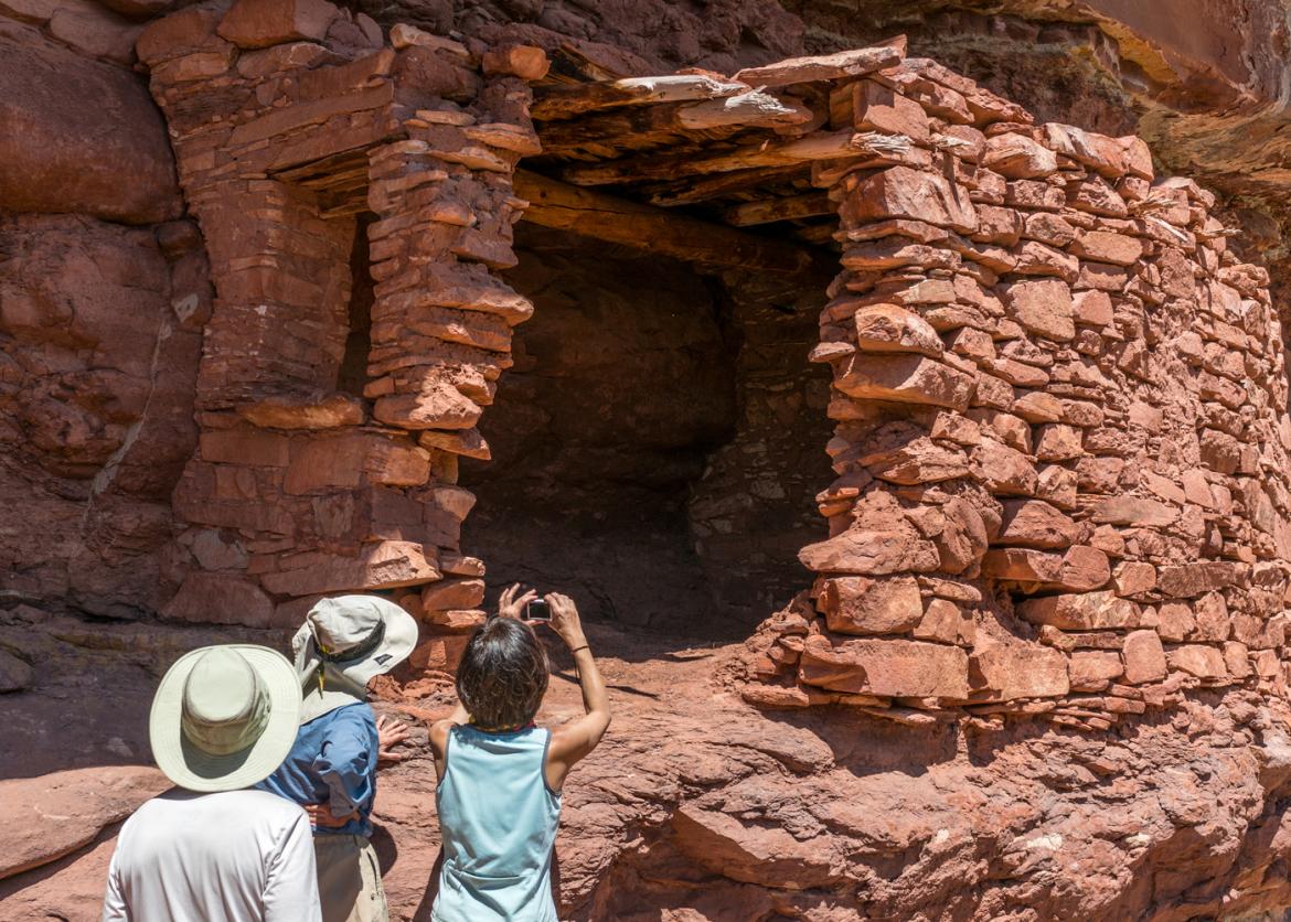 Three participants admiring and taking photos of Native American dwelling in Dark Canyon, Utah