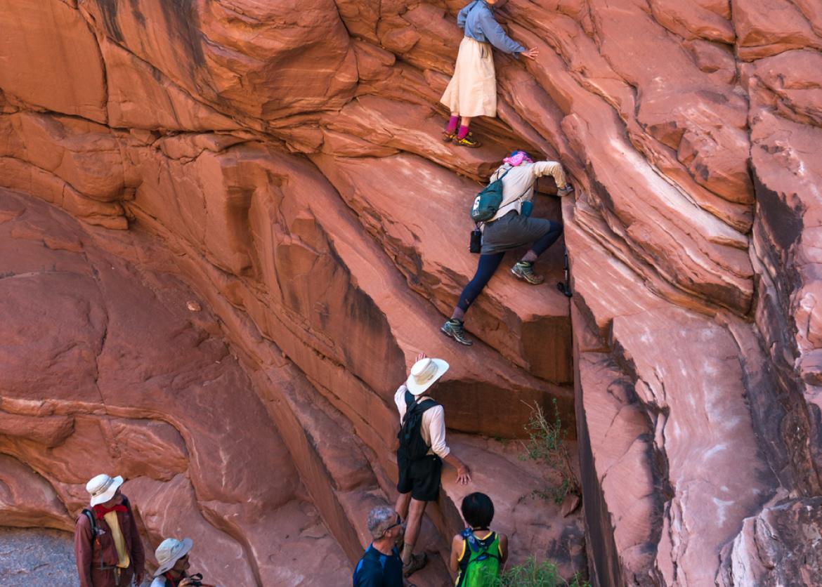 Trip participants scrambling up red rock canyon wall in Dark Canyon, Utah