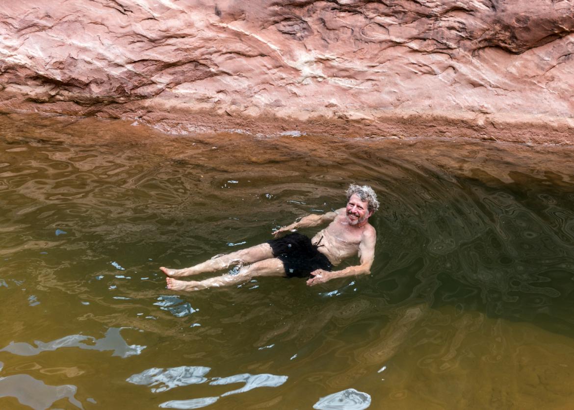 Male trip participant swimming in natural plunge pool in Dark Canyon, Utah