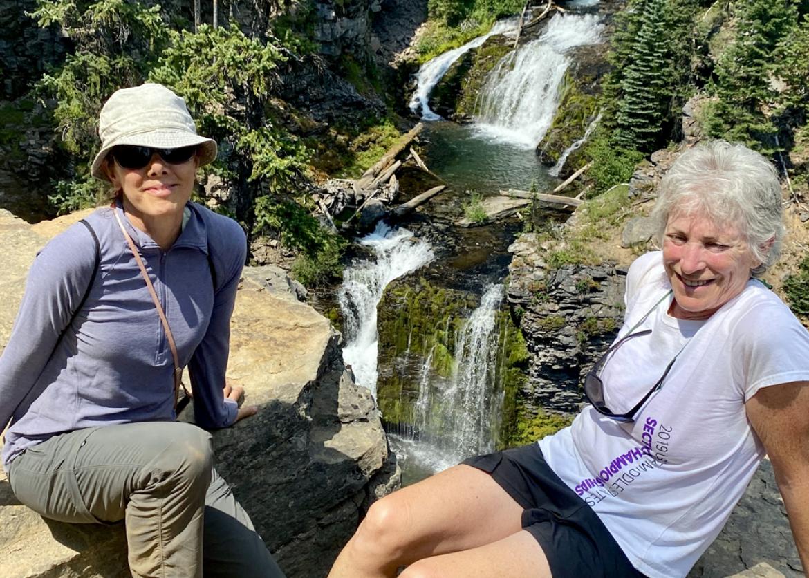 Two women chilling on the cliff with a view of the waterfall.