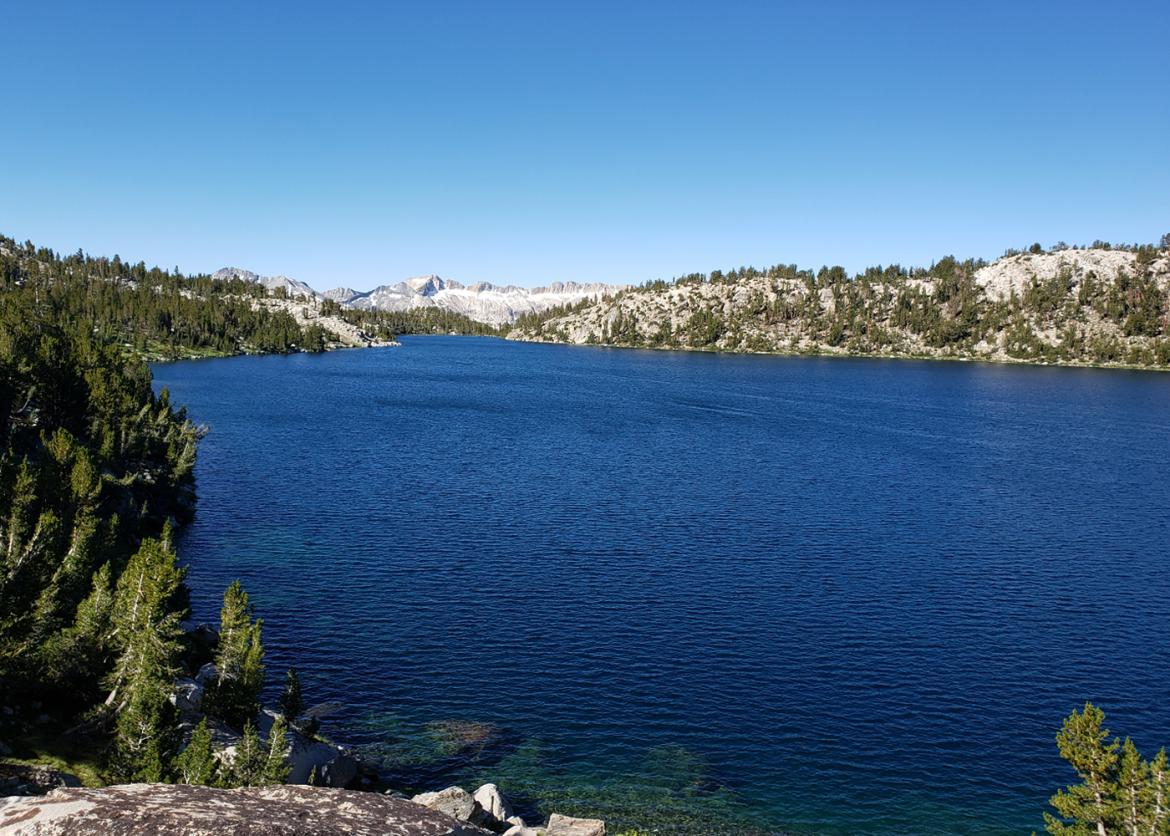 A wide shot of the deep blue lake with trees and mountains surrounding it