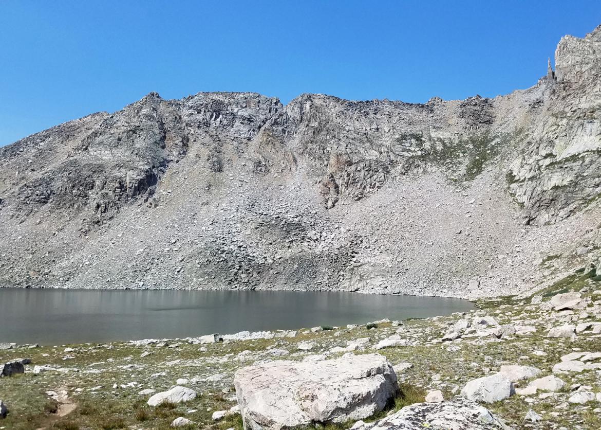 A gray mountain with a sandy texture and a lake underneath it.