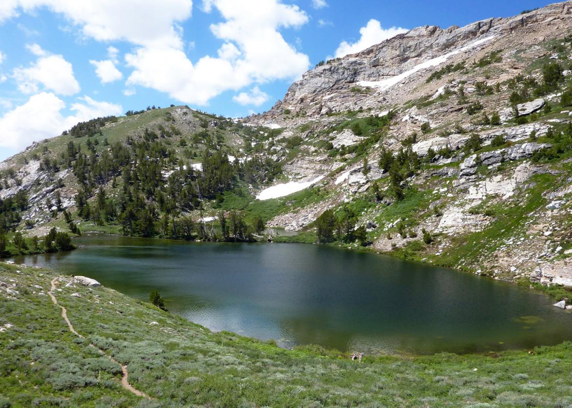 A lake in the mountains surrounded by grass and snow.
