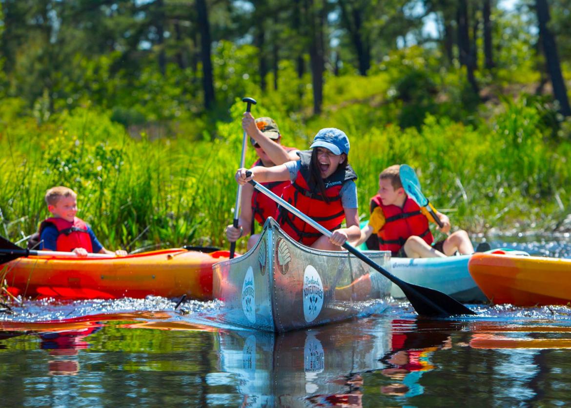 Two people in a canoe paddle away from a pair of children in inflatable rafts.
