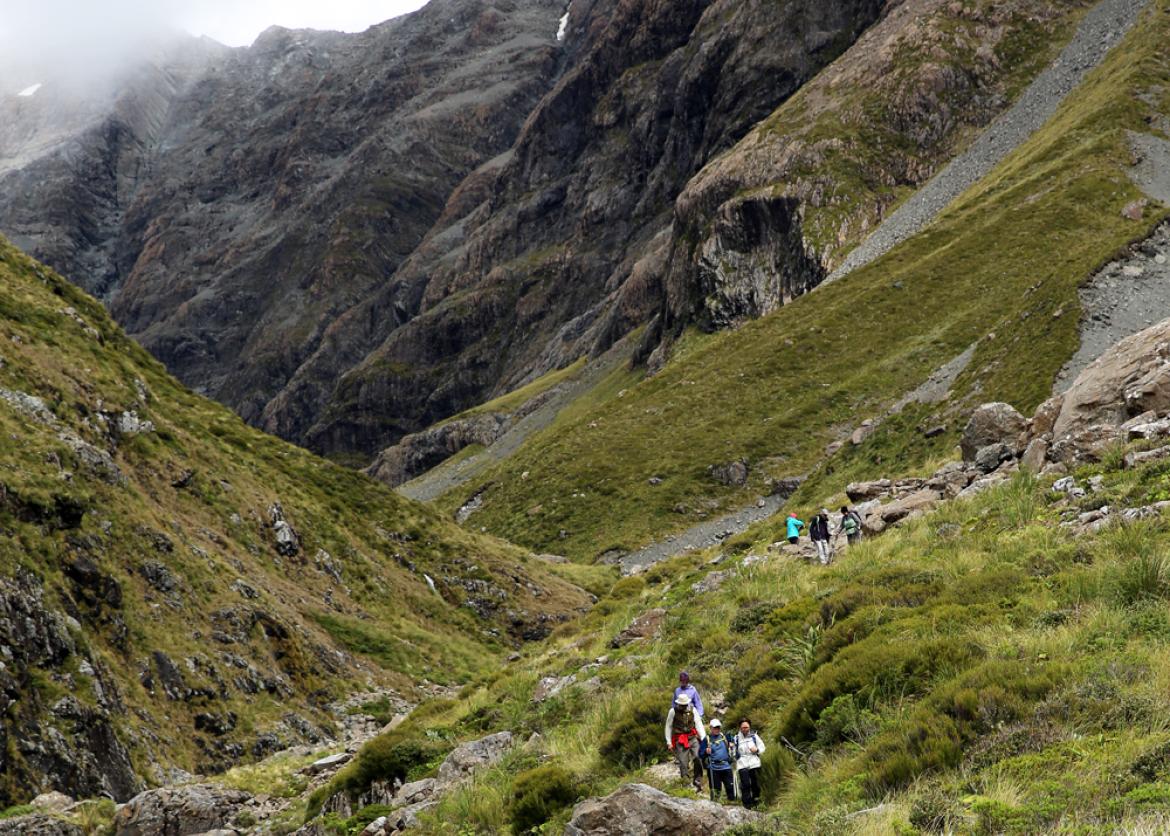 Hikers walk uphill in a grassy valley.