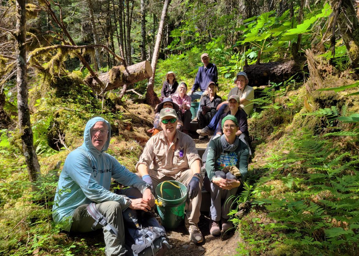 Smiling trip participants sitting on a trail in a lush green forest