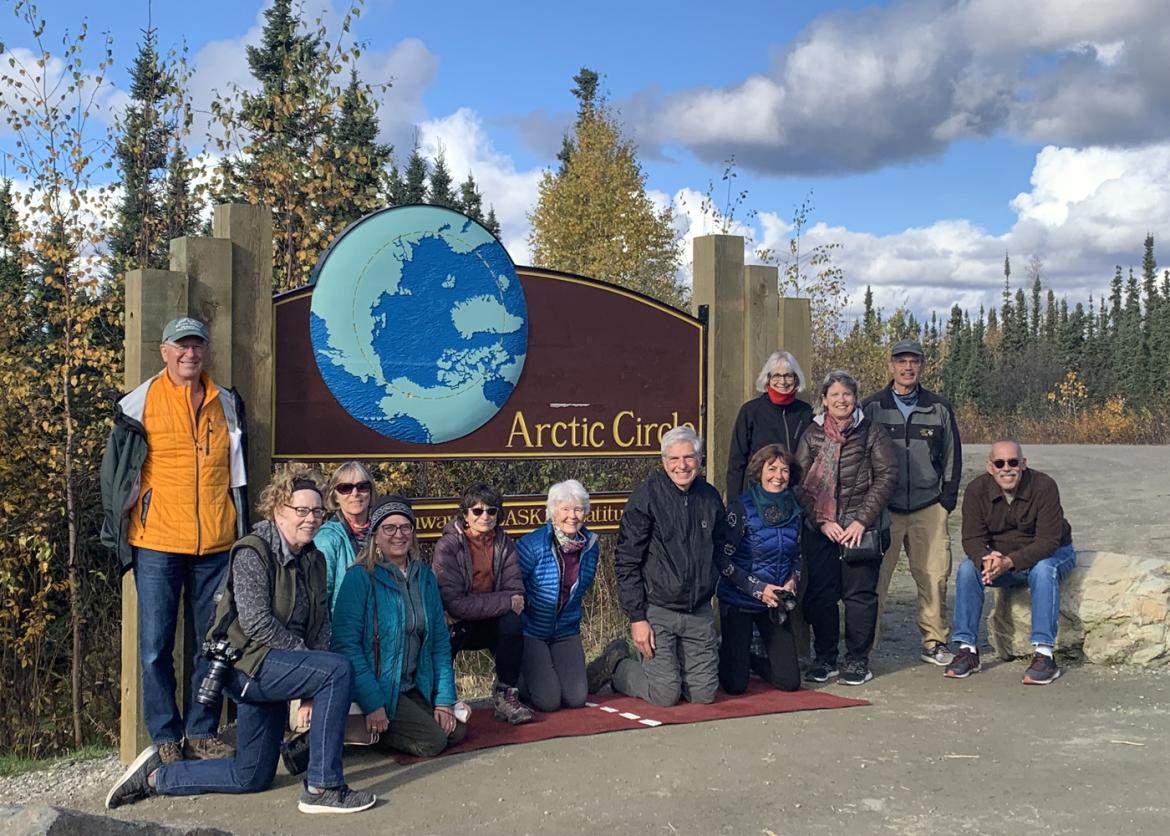 Twelve smiling participants pose in front of a sign reading "Arctic Circle."