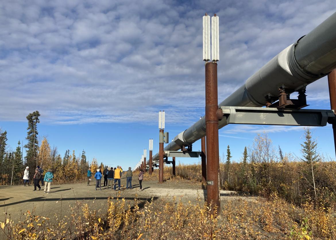 Grouped participants dwarfed by an oil pipeline held aloft on metal girders.