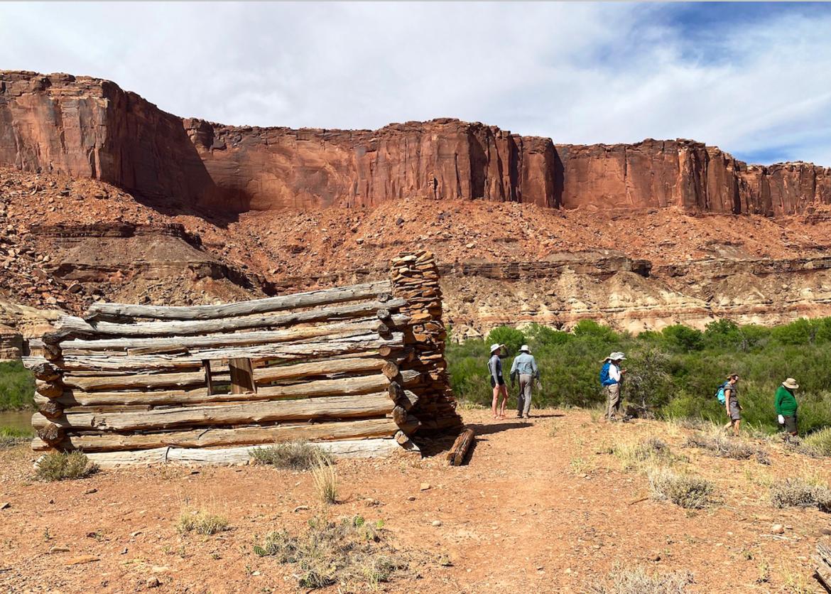 Several people hike past a building made of stacked wood.