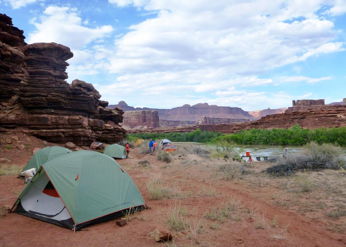 A riverside campsite where people walk between tents.