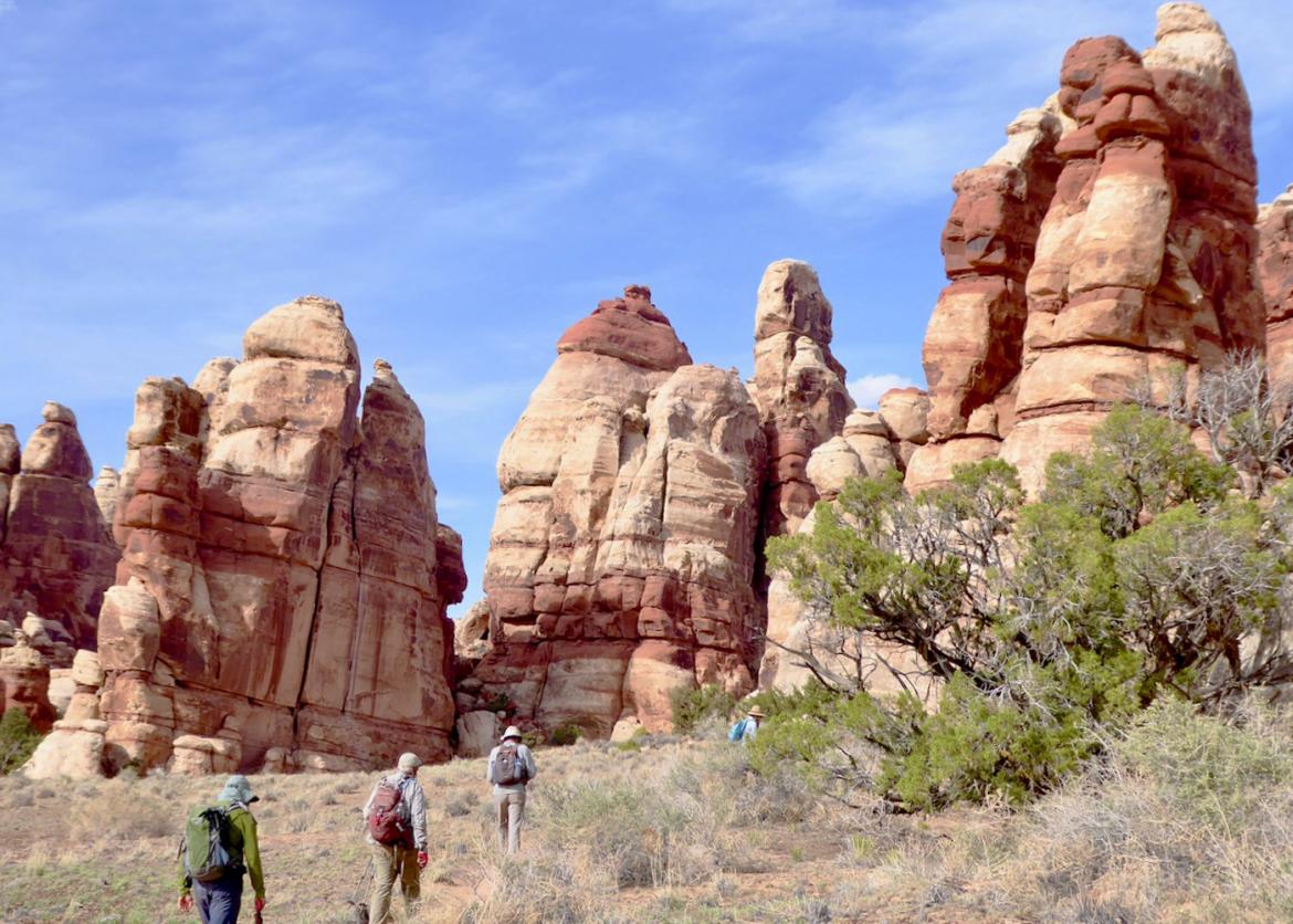 Four hikers walk towards tall rocky outcroppings.