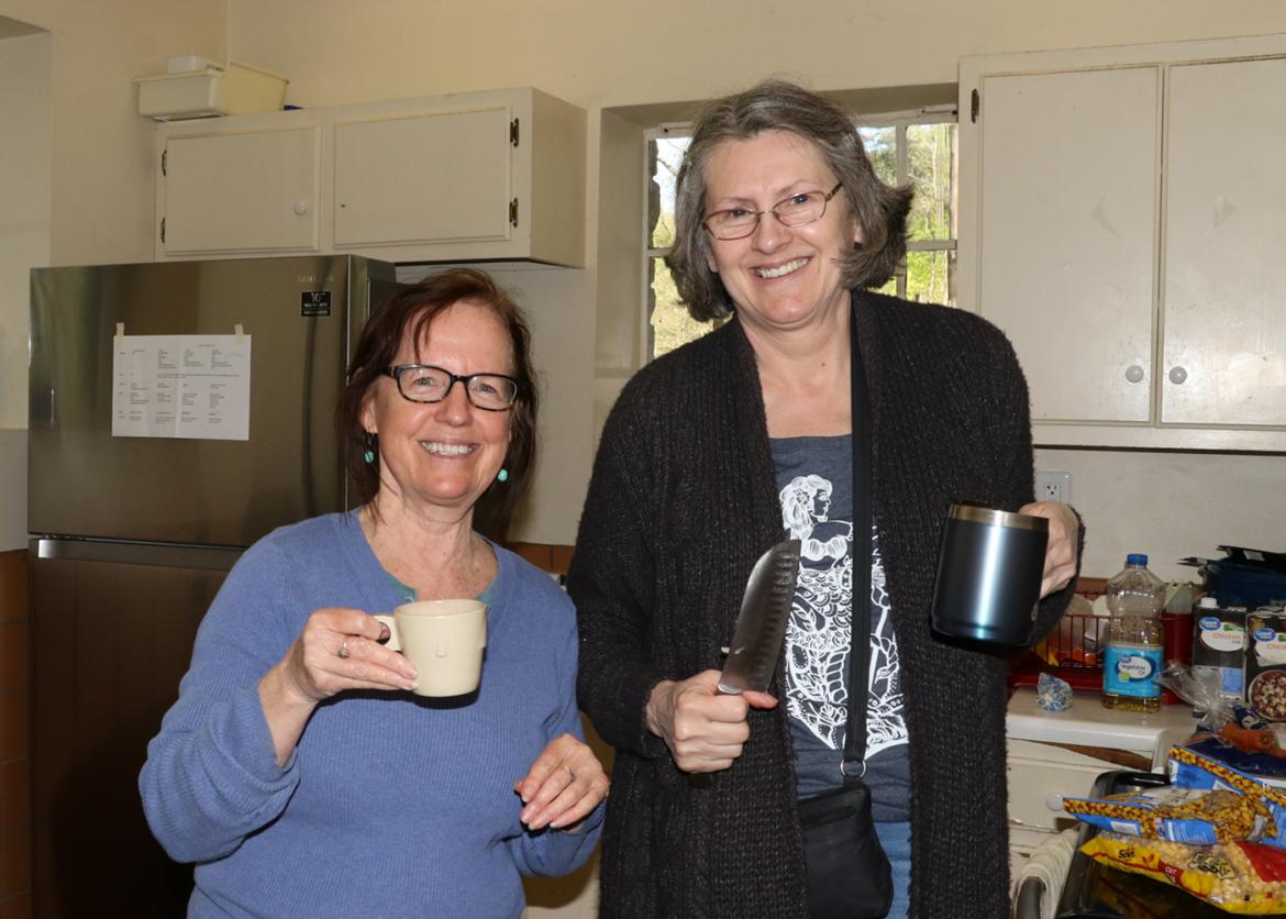 Two smiling women holding mugs in a kitchen.