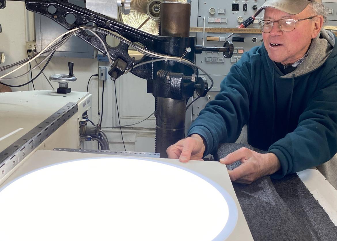 A man with glasses looking down, observing a machine with circular, bright white light coming out of it