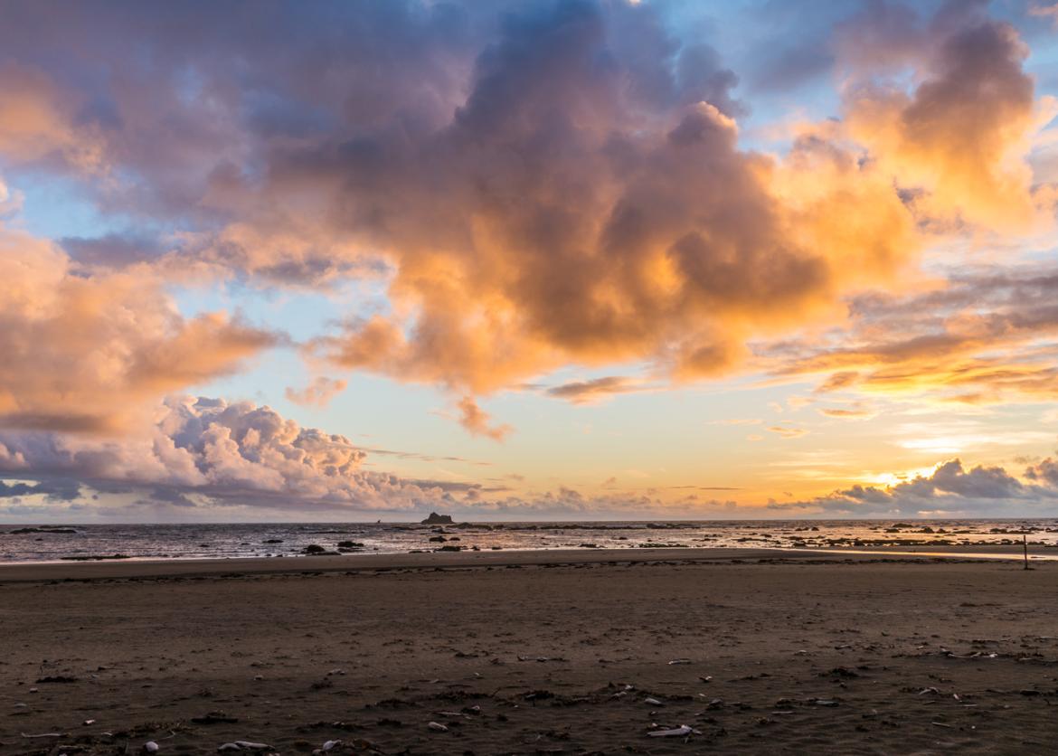 A view of a beach under a colorful clouded sky.