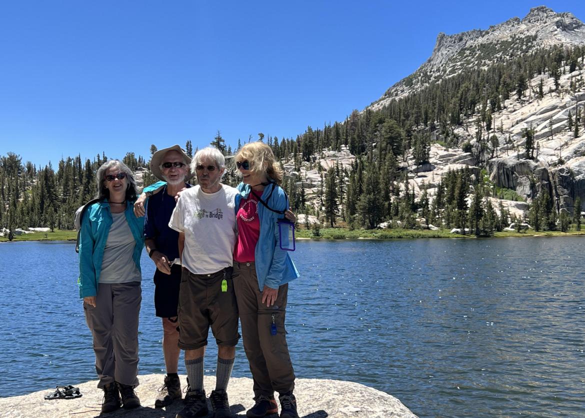 Four smiling people stand in front of a crystal lake and a tree covered mountain slope.