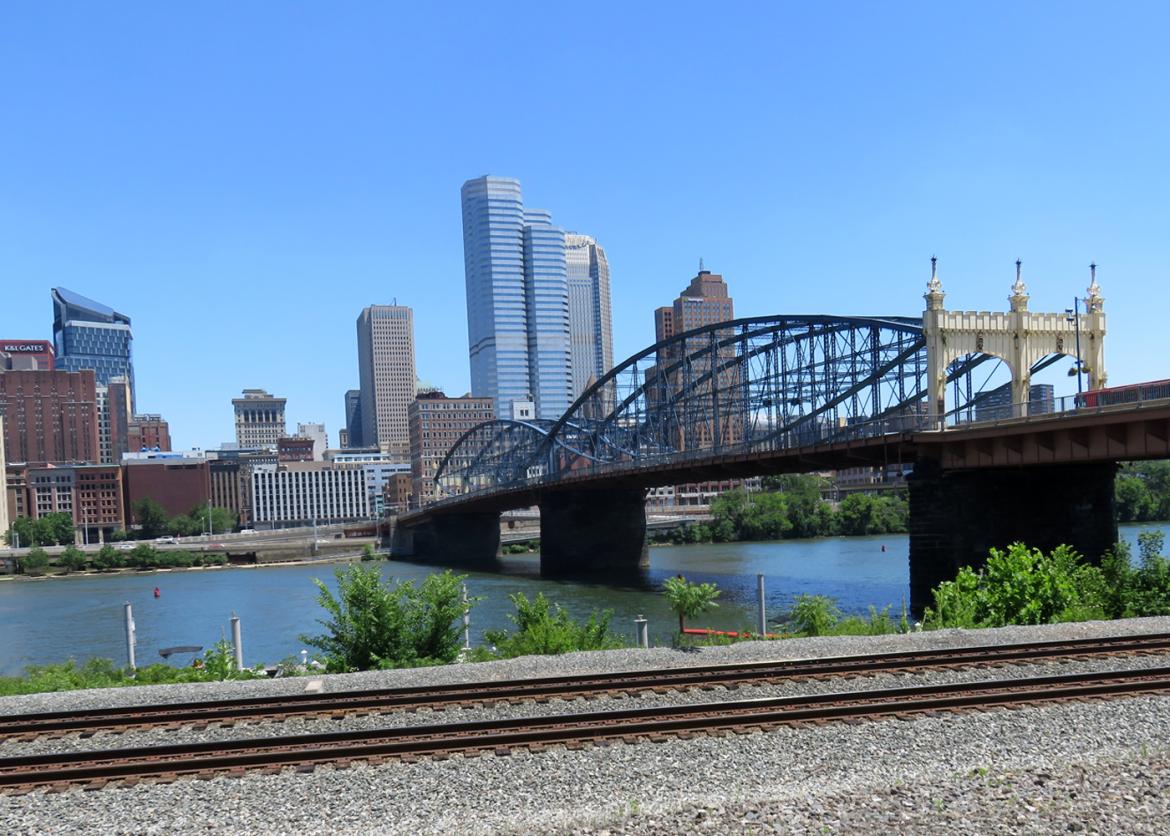 A train track with a view of the river, bridge, and buildings