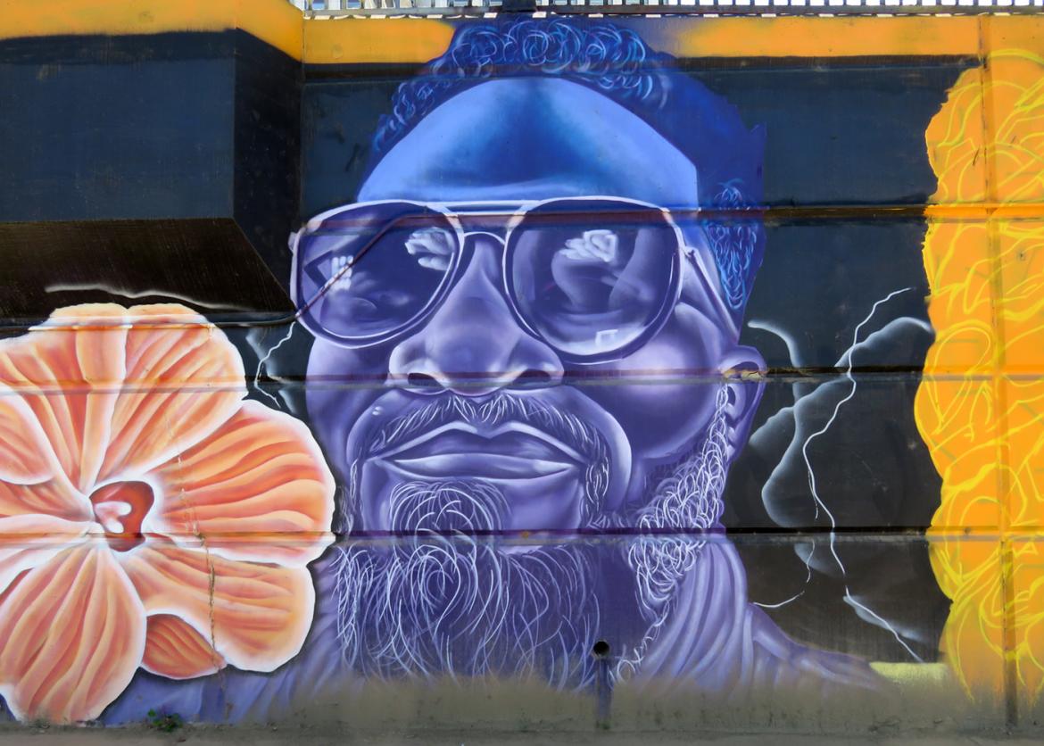 A mural of a man in sunglasses in purple and blue smiling