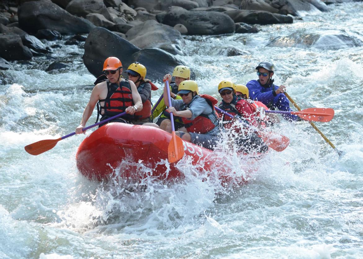 A group of people wearing life jackets and helmets rafting