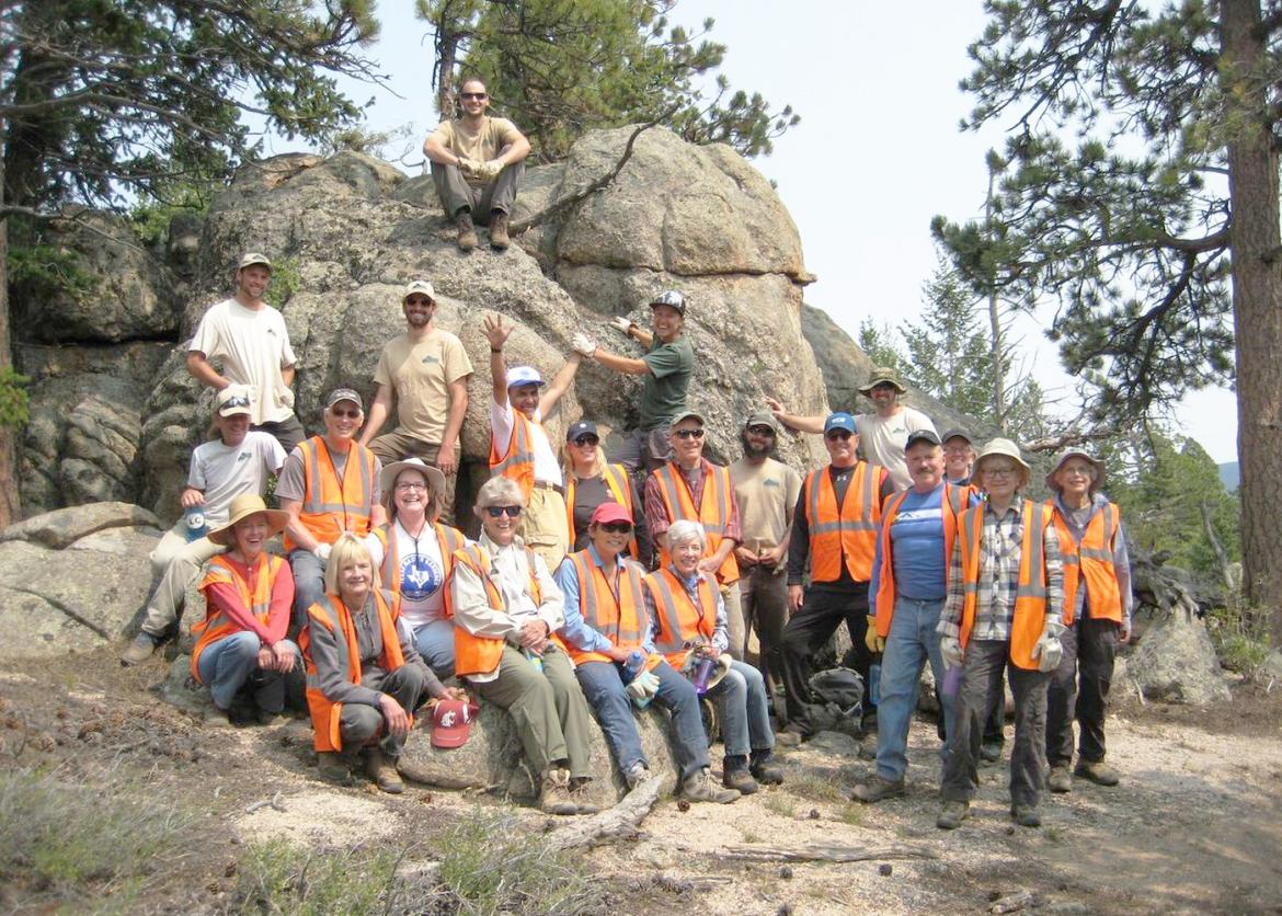 A group of twenty-two smiling people, most wearing orange high visibility vests. 