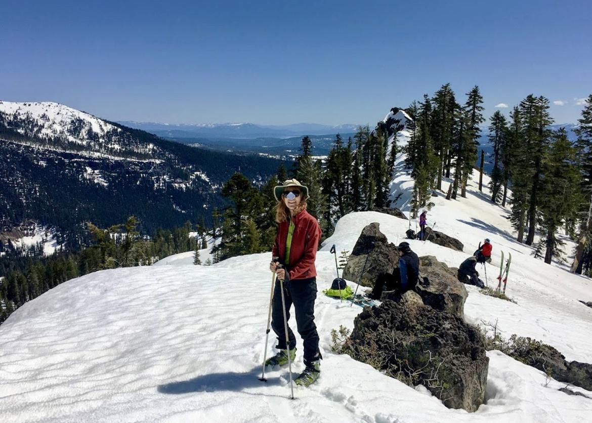Woman smiling while four people behind her take a rest from backcountry skiing down the snow-covered slopes at Lassen Volcanic National Park, California