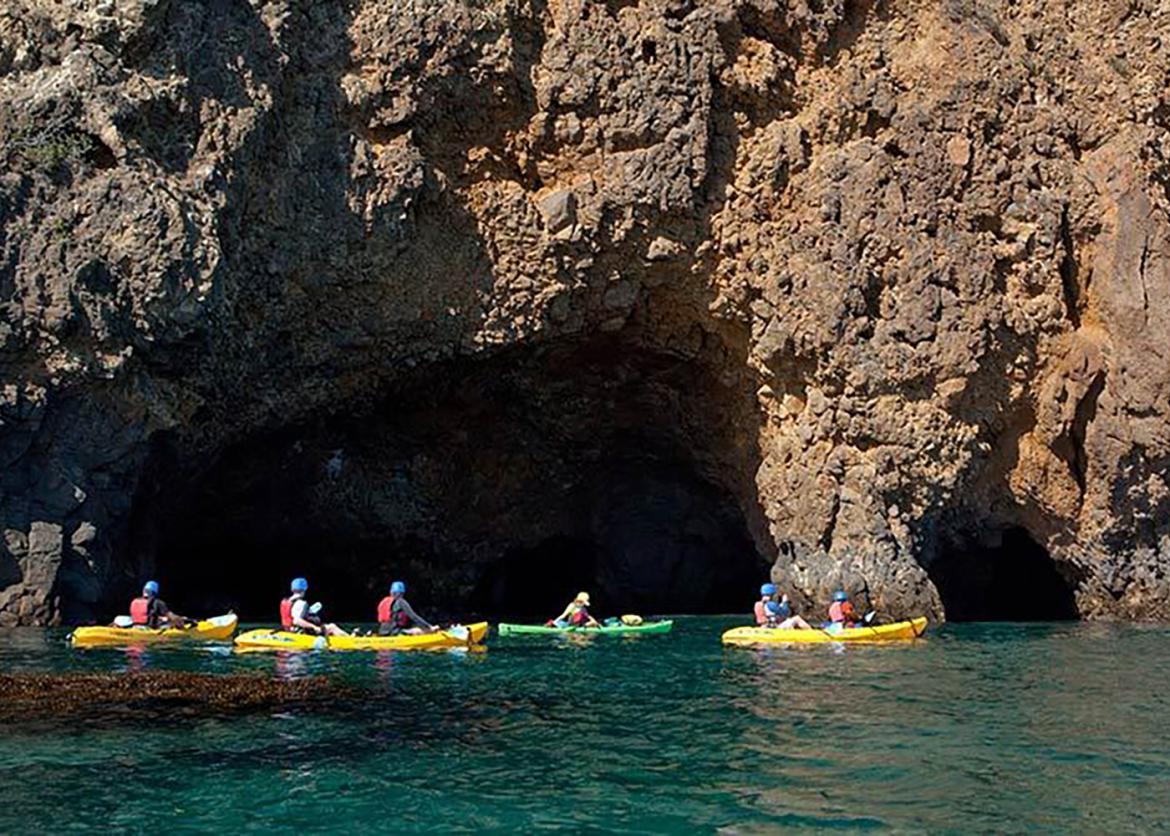 Kayakers in the Pacific Ocean next to the cliffs of Santa Cruz Island rising out of the sea