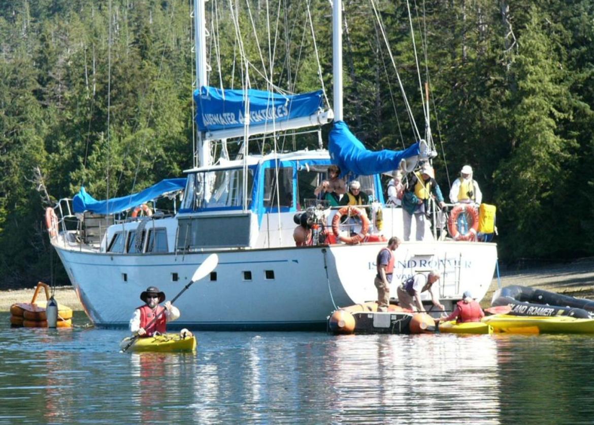 A docked boat, full of people, surrounded by inflatable rafts and kayaks.