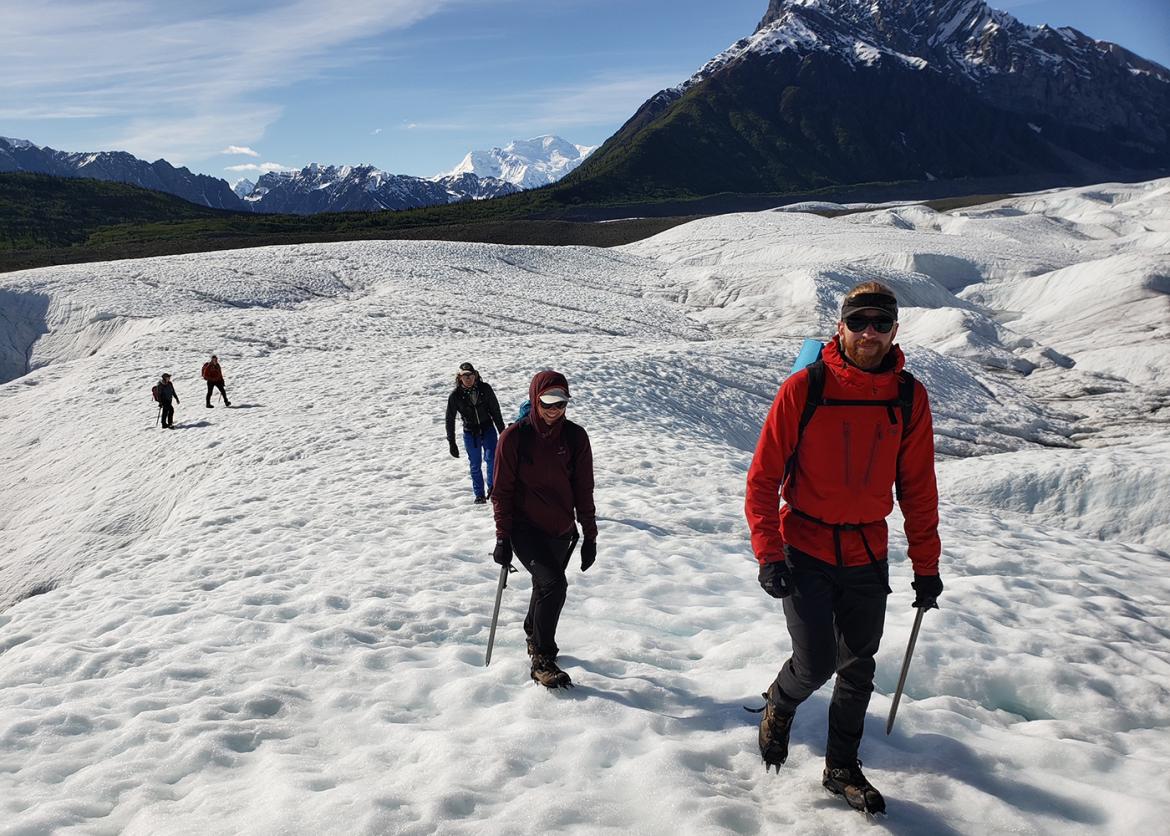 Trip participants hiking through snow with snow-covered peaks in background, Alaska
