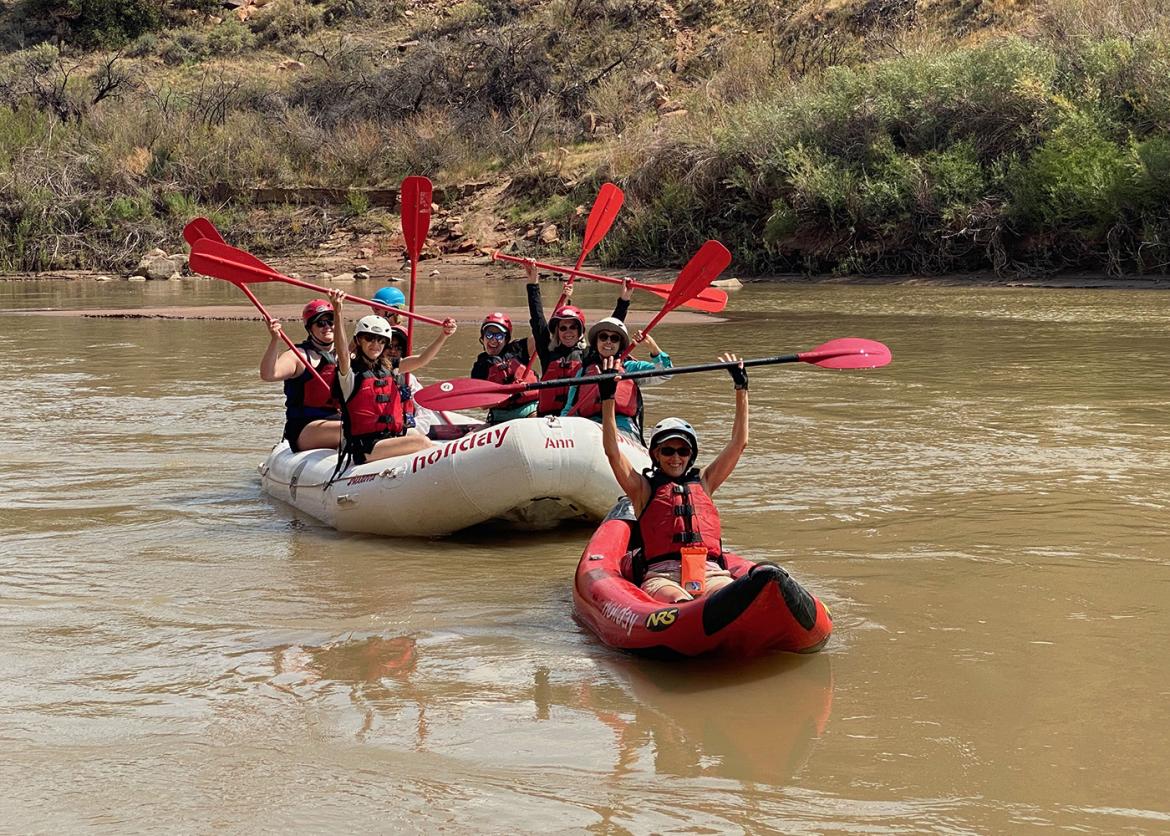 Trip participants lift their paddles up while rafting on the river