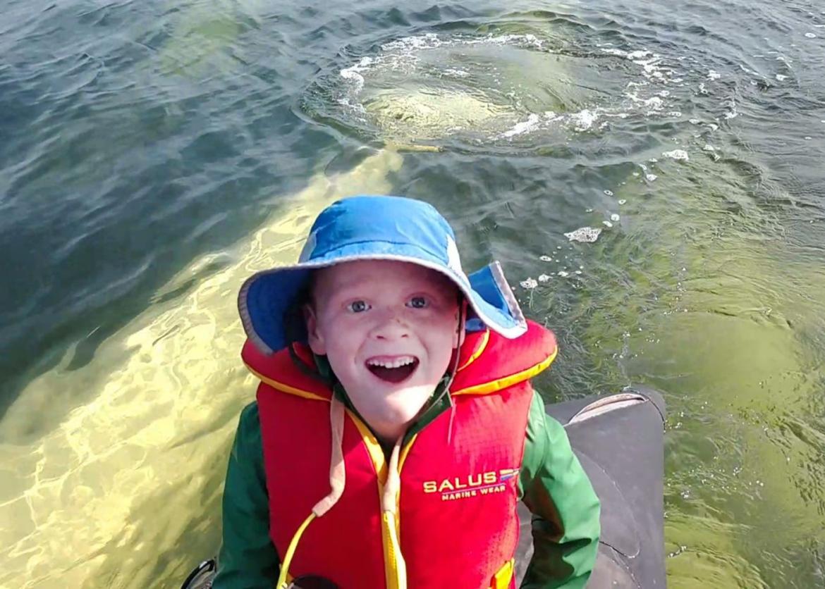 Young boy on a kayak smiling gleefully as beluga whales pass beneath in the water