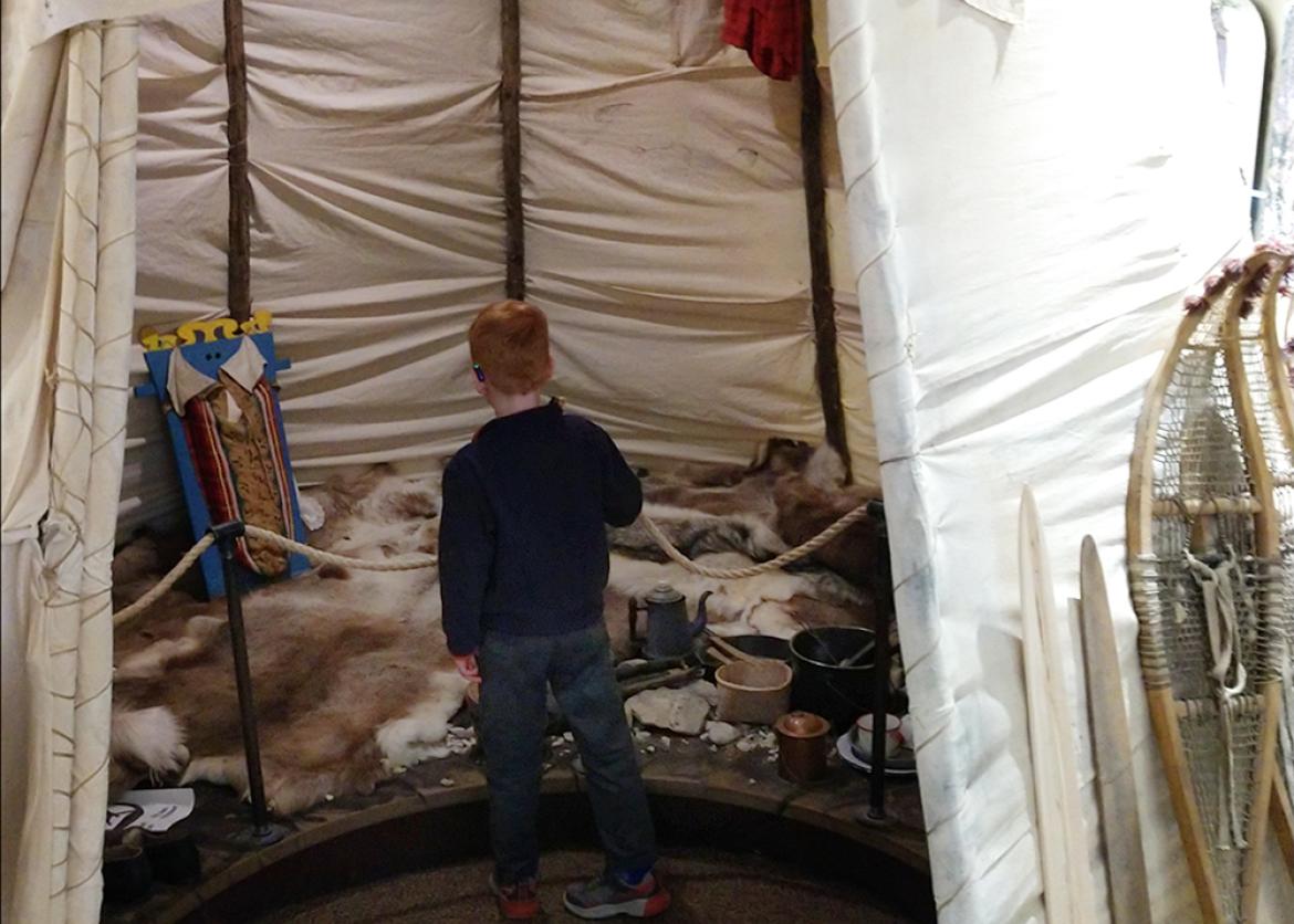 Child inside an indigenous tipi, viewing artifacts on display within