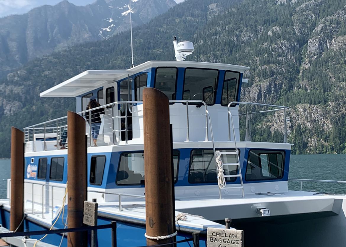 Blue ferry on lake with mountains in background