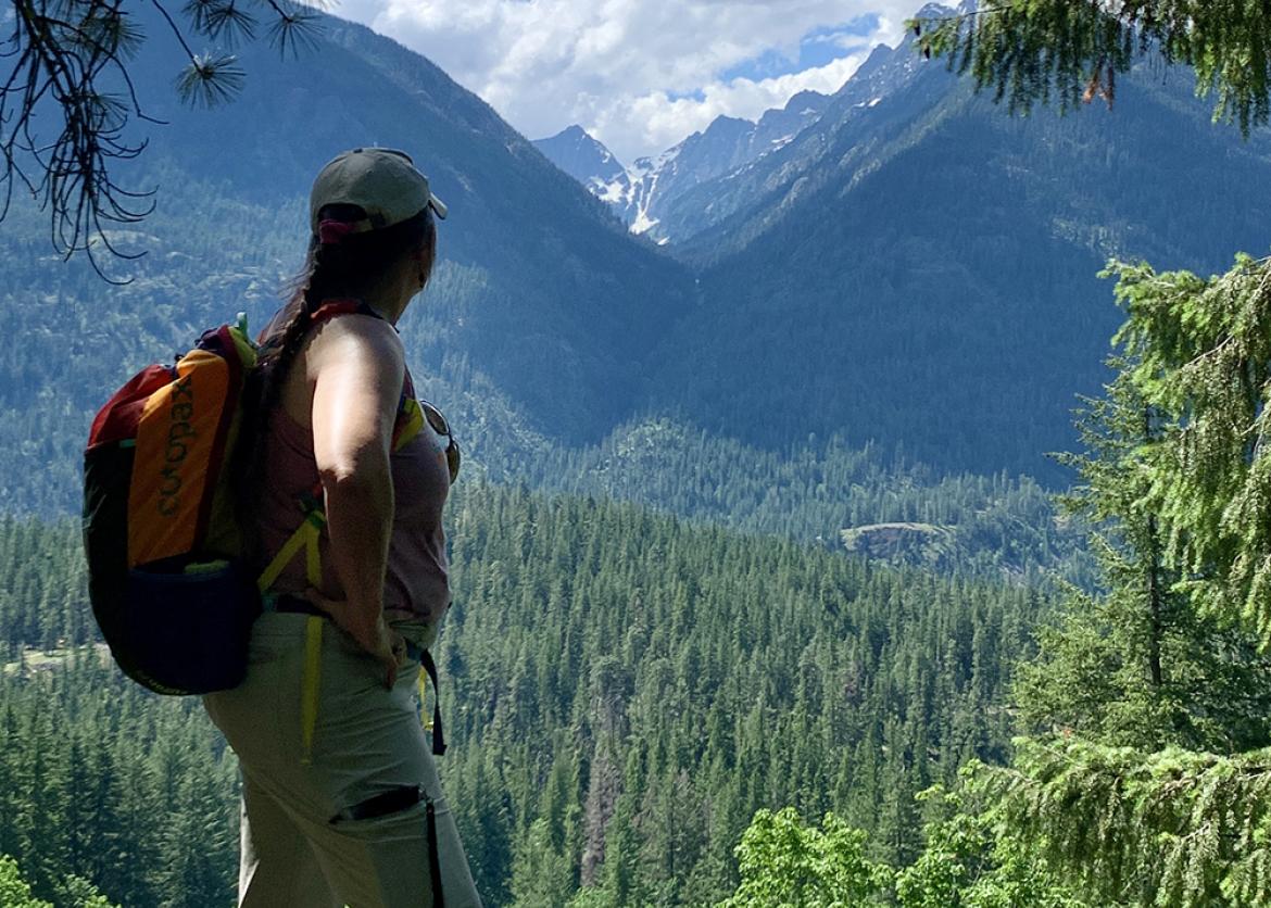 Woman pauses along hiking trail to enjoy the view of green, tree-covered mountains