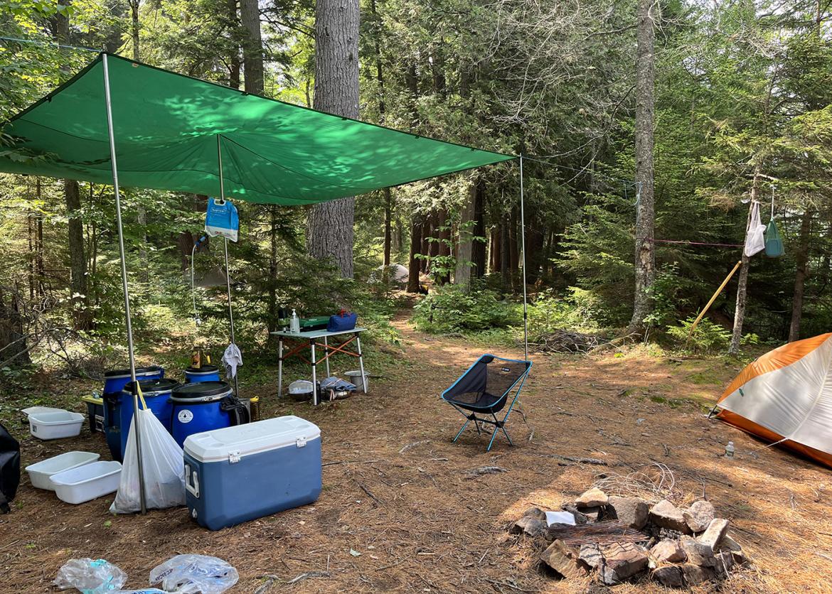 Campsite set up with tent, fire ring, chair, and tarp shelter