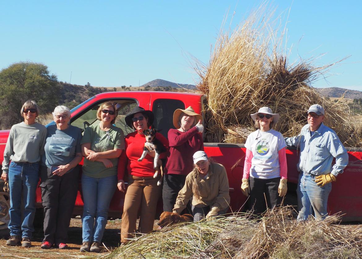 Workers and a puppy pose in front of a truck loaded with dry straw.