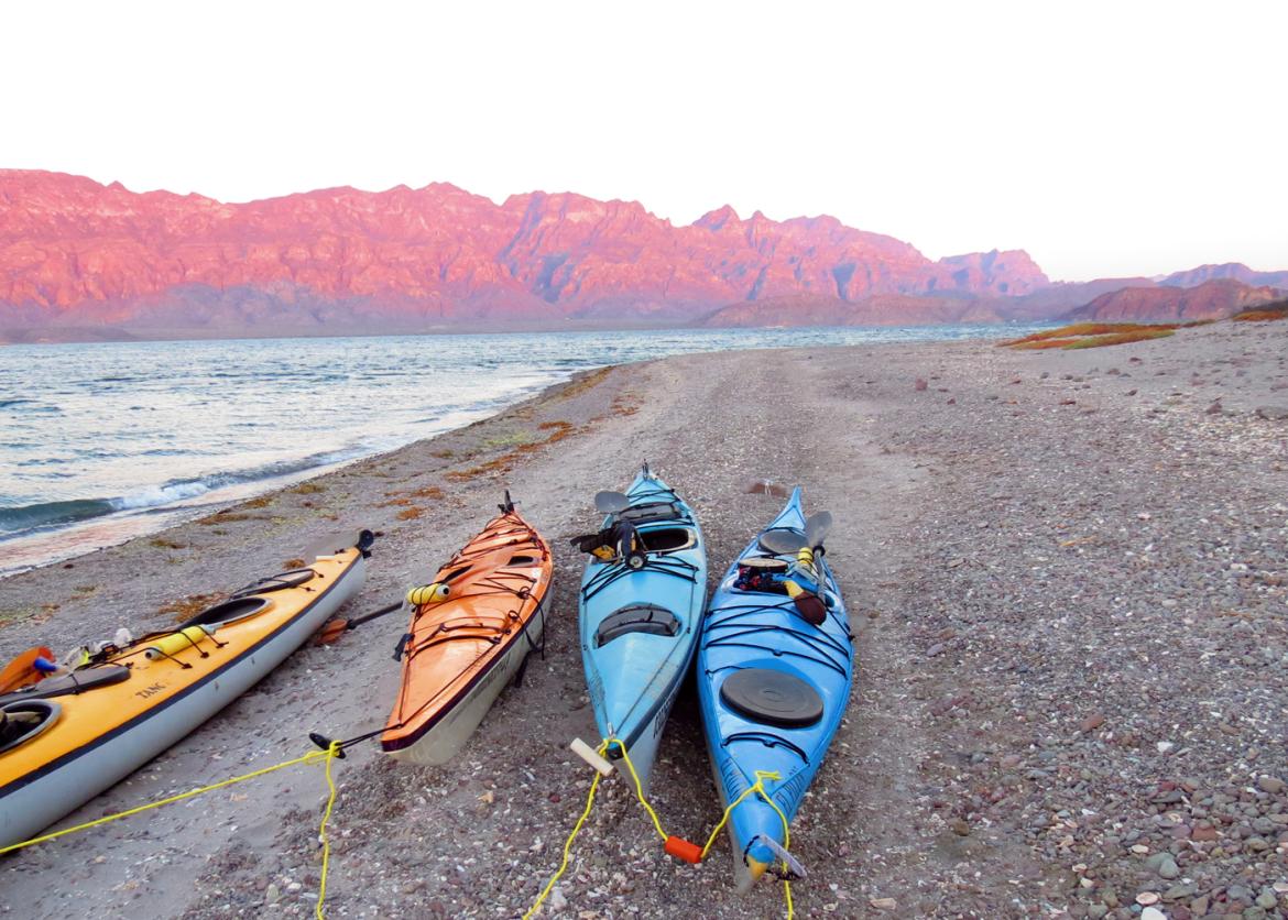 Four kayaks resting on a pebbled shore.