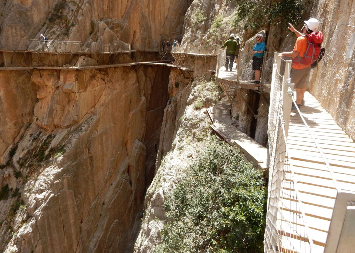 People on a walkway look around from their vantage high up on a sheer canyon wall.
