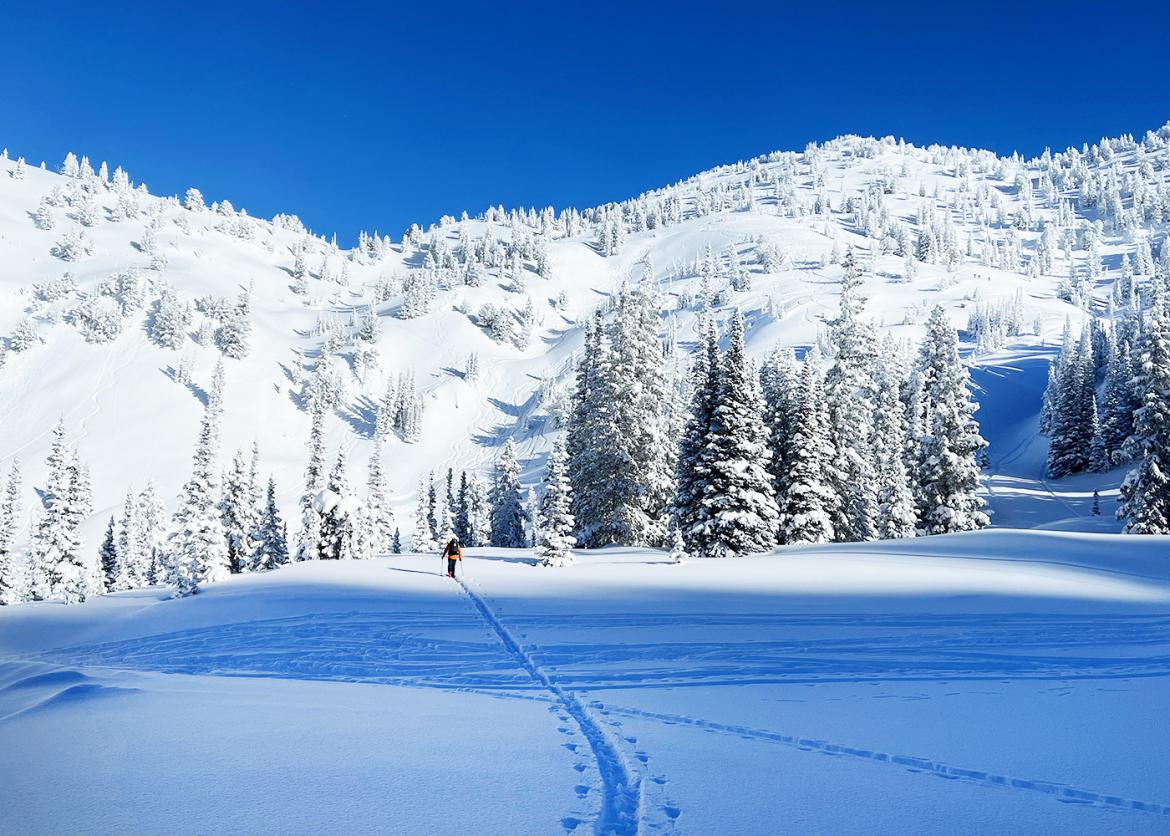 A person goes on a ski run across flat ground towards a snowy ridge.