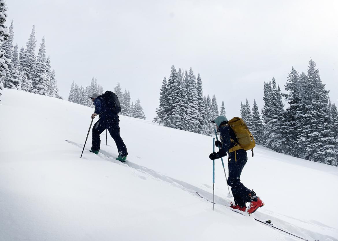 Two people use ski poles to go uphill on a snowy slope.