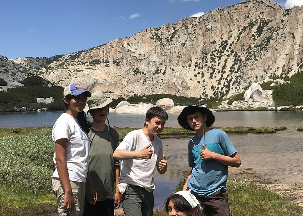Group of teen participants pose for the photo in front of lake and mountain peak.