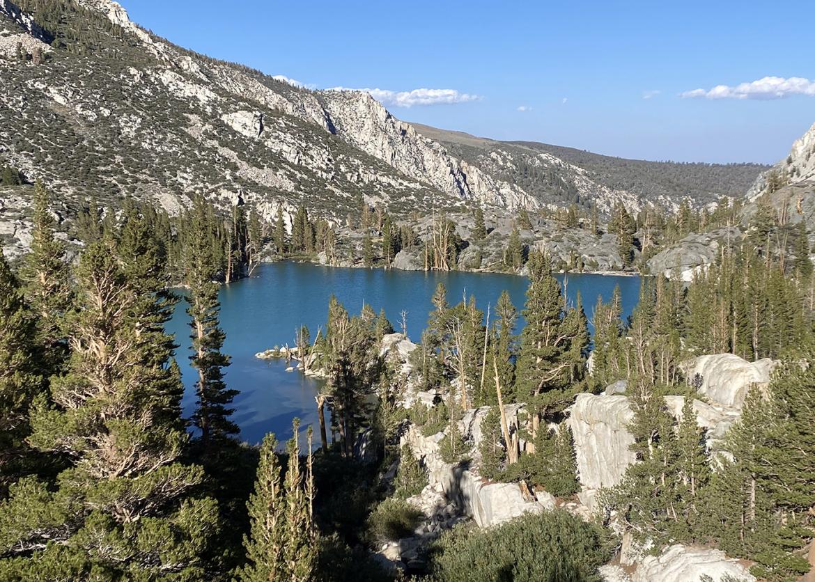 A blue lake against a mountainous backdrop with evergreen trees in the foreground