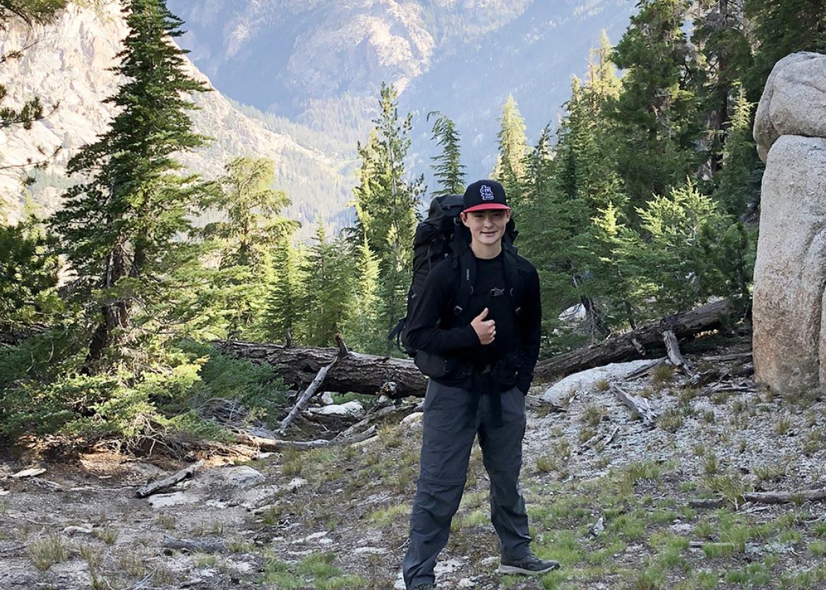 Trip participant smiles for camera with mountain scenery in background.