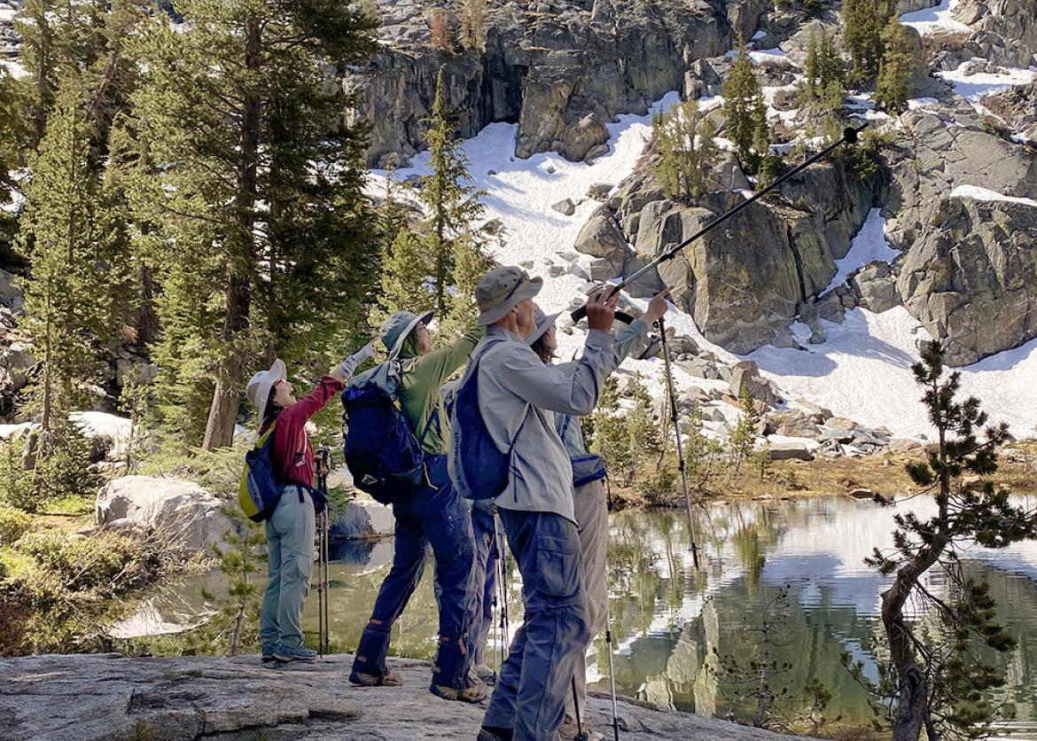 Trip participants take in the view and point with their hiking poles by a lake and mountainside in yosemite