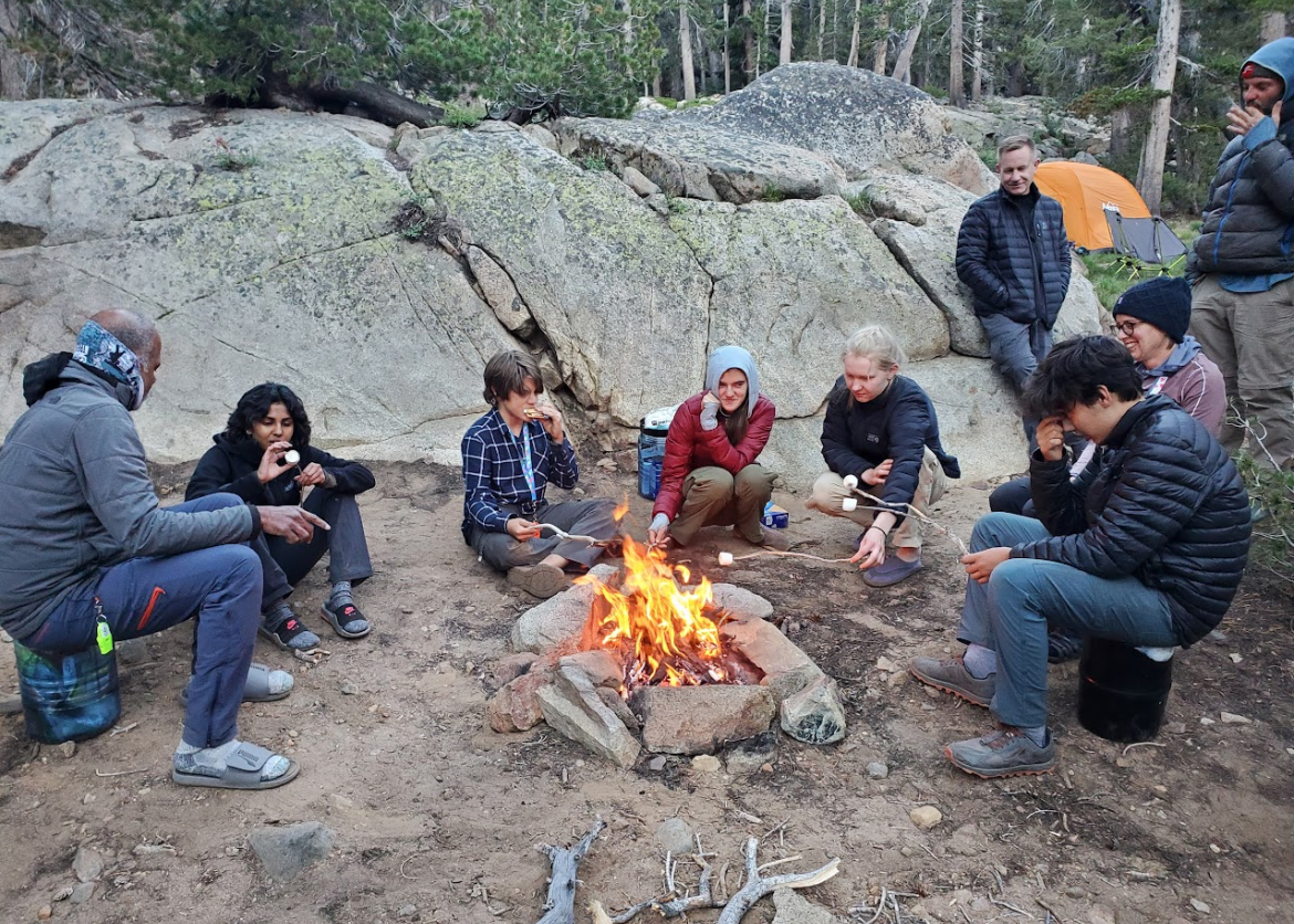 A group of teens and adults surrounding the campfire, making s'mores