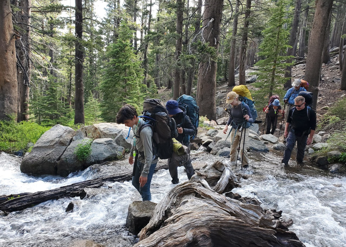 A group of teens and adults crossing the stream in line